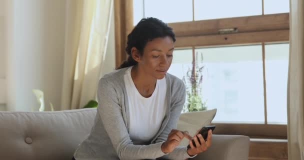 Joven mujer africana usando aplicaciones móviles en el teléfono en casa — Vídeo de stock