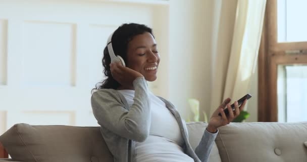 African woman wearing wireless headphones relaxing listening music on phone — Stock Video