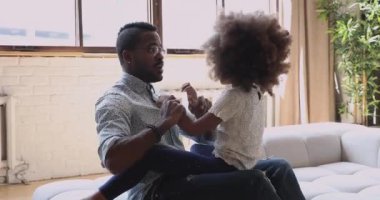 Afrikalı baba kanepenin üzerinde sevimli kız çocuğuyla güler.