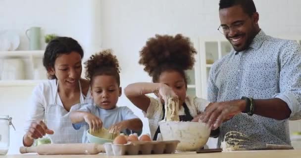 Милые маленькие африканские дети месят тесто, помогая родителям на кухне. — стоковое видео