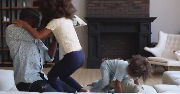 Despreocupado papá africano y los niños jugando pelea de almohadas en el sofá — Vídeo de stock