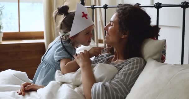 Grappig kind meisje doen alsof arts check moeder keel in slaapkamer — Stockvideo