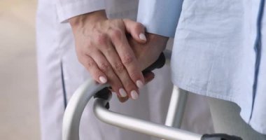 Yaşlı bir hastanın elini tutan kadın hemşire yürüyüş çerçevesi kullanıyor, yakın plan.