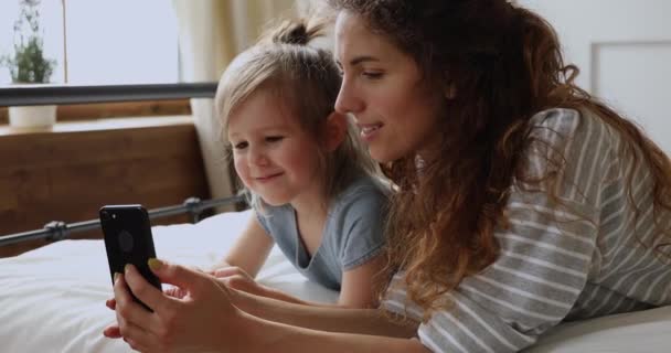 Mãe feliz com filha criança gosta de usar o telefone na cama — Vídeo de Stock