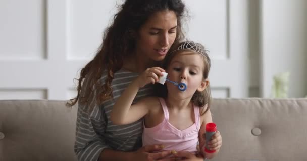 Счастливая мама играет с дочерью надувая мыльные пузыри дома — стоковое видео
