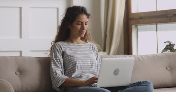 Mosolygó fiatal nő ül a kanapén gépelés a laptopon — Stock videók