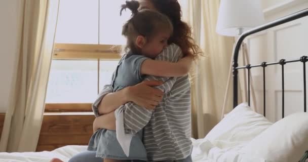 Щаслива мати обіймає милу маленьку доньку, яка грає на ліжку — стокове відео