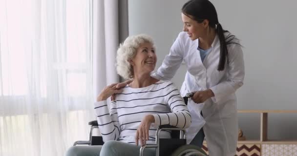 Молодая женщина сиделка разговор помочь старшей бабушке на инвалидной коляске — стоковое видео