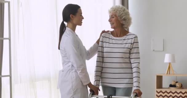 Žena pečovatel pomáhá šťastný starý zdravotně postižený babička stojí držet Walker — Stock video