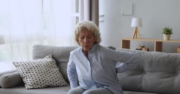 Zdenerwowana starsza kobieta czuje ból pleców wstając z sofy — Wideo stockowe