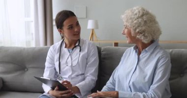 Mutlu yaşlı hasta ve kadın hemşire tıbbi ziyaret sırasında konuşuyor.