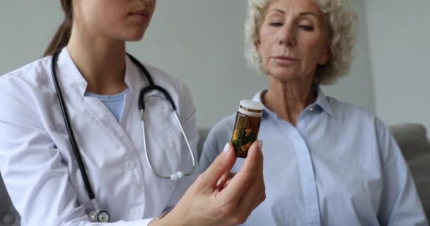 Kadın doktor eczacı yaşlı hastaya ilaç şişesi yazıyor. — Stok video