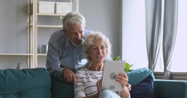 Mosolygó idős pár beszél táblagéppel otthon — Stock videók