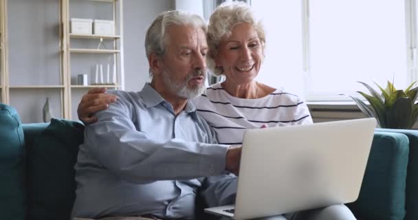 Літня сім'я і бабуся і дідусь розмовляють за допомогою ноутбука сидять на дивані — стокове відео
