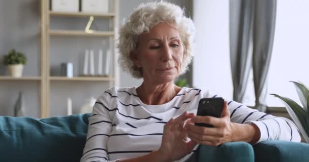 La nonna dai capelli grigi più anziana che usa le app mobili siede sul divano — Video Stock