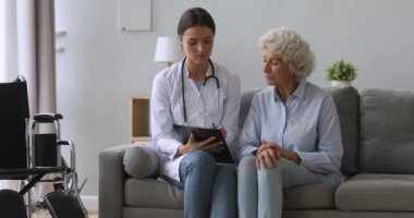 Genç kadın doktor, engelli yaşlı hastaya panoya yazmasında yardım ediyor.