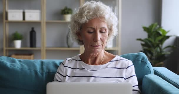 Счастливая пожилая женщина использует ноутбук, глядя на экран — стоковое видео