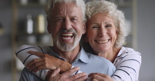 Веселая пожилая пара обнимается смеясь, сближаясь глядя в камеру — стоковое видео