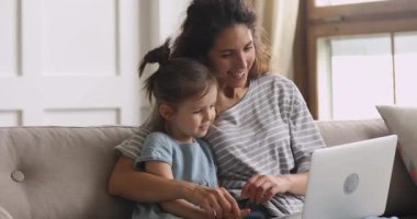 Mutlu anne ve anaokulu kızı birlikte dizüstü bilgisayar kullanarak eğleniyorlar.