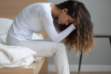 Mutsuz, melez, yatakta oturan, depresyonda olan genç bir kadın..