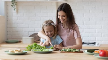 Gülümseyen anne küçük kızına mutfakta bıçak kullanmayı öğretiyor.