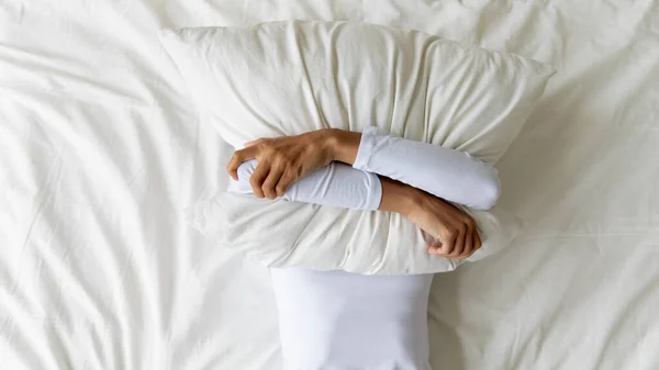 Young girl lying on bed, covering face with pillow. — Stock Photo, Image