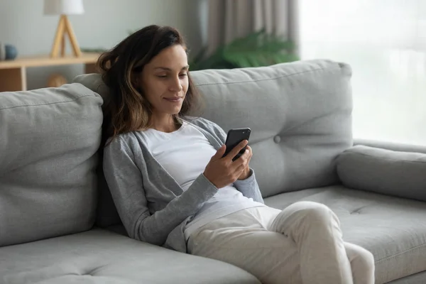 Peaceful mixed race girl relaxing on comfortable sofa with phone. — ストック写真