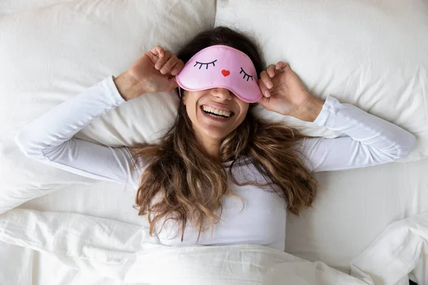 Glückliche Millennial-Frau liegt mit Schlafmaske im Bett. — Stockfoto