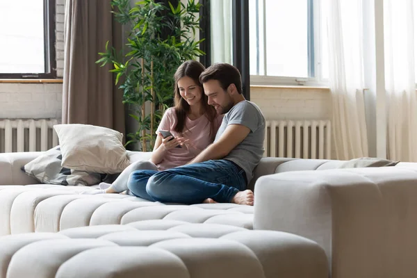 Happy couple in love relaxing on couch, using phone together — ストック写真