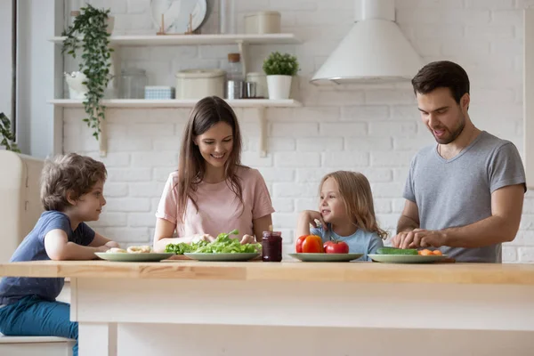 Lyckliga föräldrar med son och dotter förbereder middag, chattar — Stockfoto