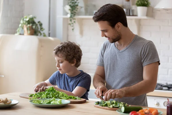 Caring father and adorable son cooking salad together in kitchen — ストック写真