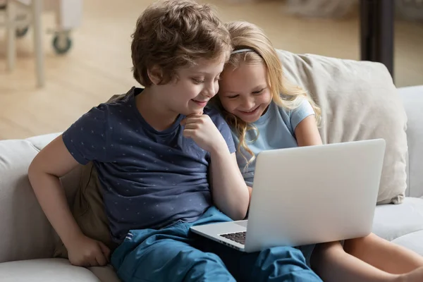 Liten pojke och flicka som använder laptop, tittar på tecknade serier eller spelar — Stockfoto