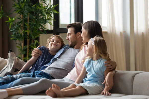 Щаслива сім'я, мати, батько і діти обіймаються, розслабляючись на дивані — стокове фото