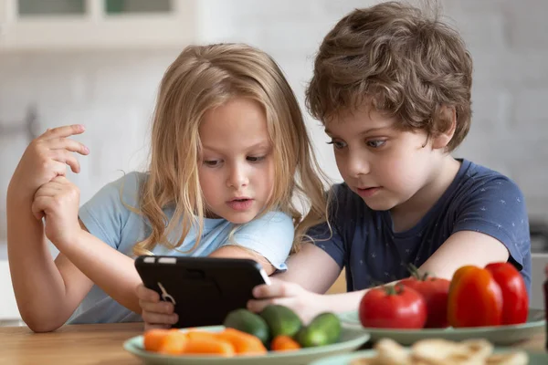 Nyfiken liten flicka och pojke använder telefon i köket — Stockfoto