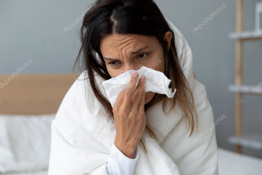 Unhealthy millennial mixed race girl wiping runny nose.
