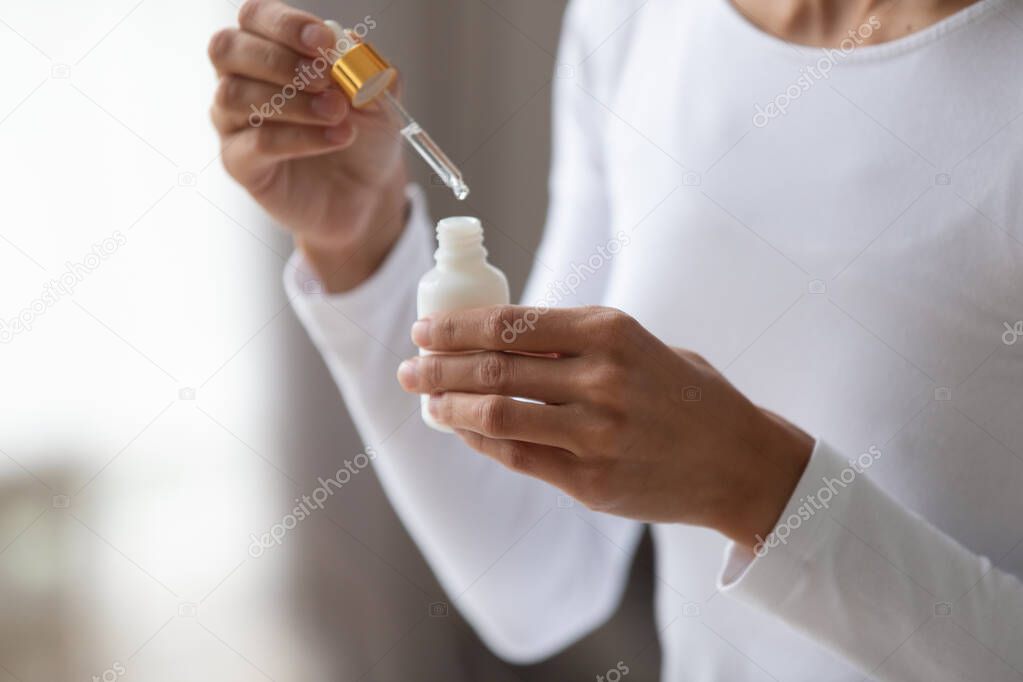Close up young woman holding bottle with pipette.