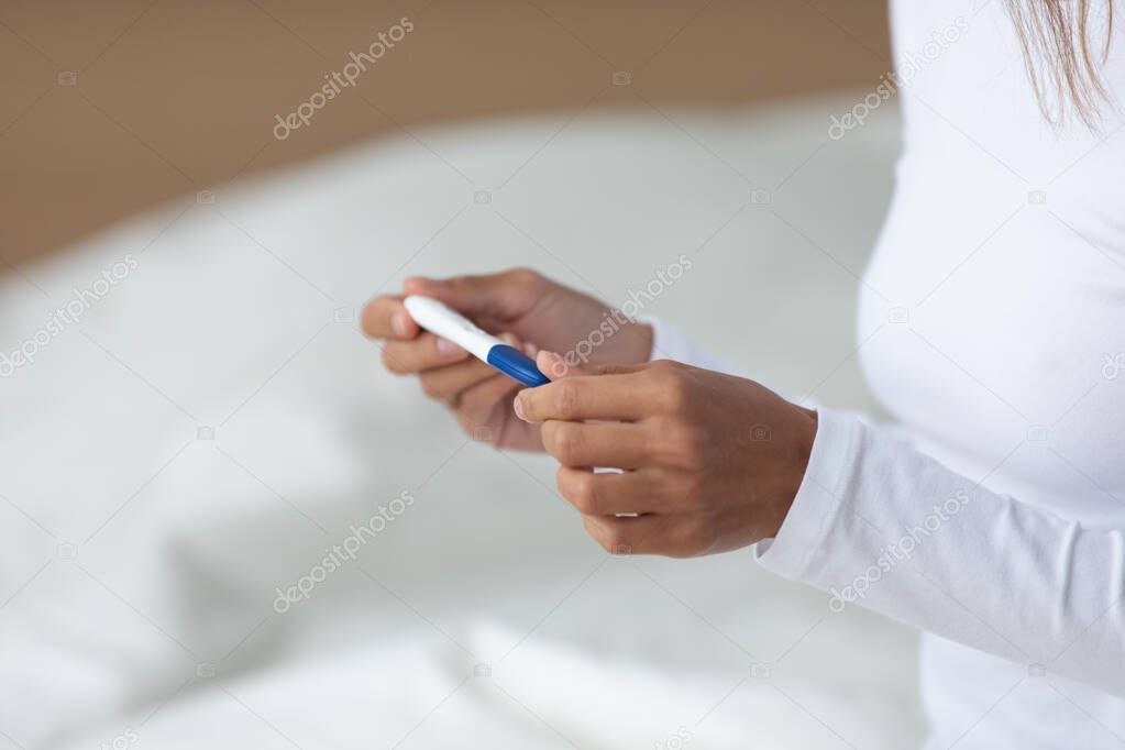 Young mixed race woman holding quick plastic pregnancy test in hands.