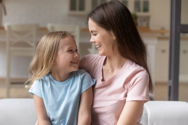 Gülümseyen anne ve küçük kız sarılıyorlar, birbirlerine bakıyorlar.