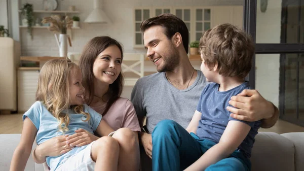 Smiling mother and father with kids sitting on couch — ストック写真