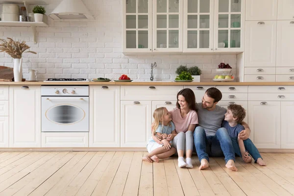 Счастливая семья с детьми, сидящими на полу в современной кухне — стоковое фото