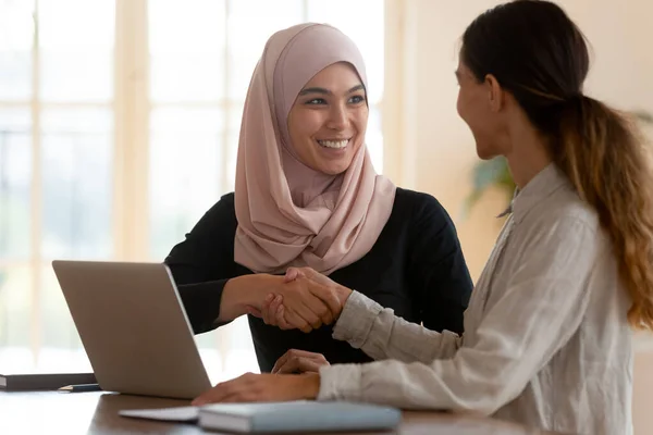 Happy female asian muslim manager handshaking caucasian lady client