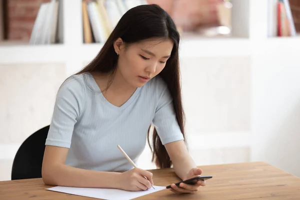 Vietnamese student using app downloaded on phone studying seated indoors — ストック写真