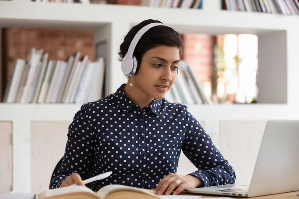 Indian dziewczyna w słuchawki zrobić zadanie w bibliotece za pomocą komputera — Zdjęcie stockowe