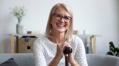 Mutlu yaşlı kadın elinde bastonla kameraya bakıyor.