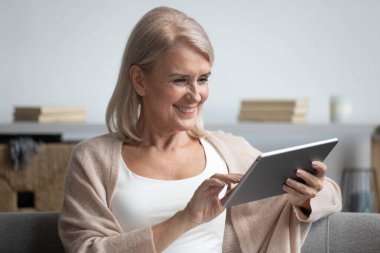 Evde tablet bilgisayar kullanan mutlu orta yaşlı kadın.