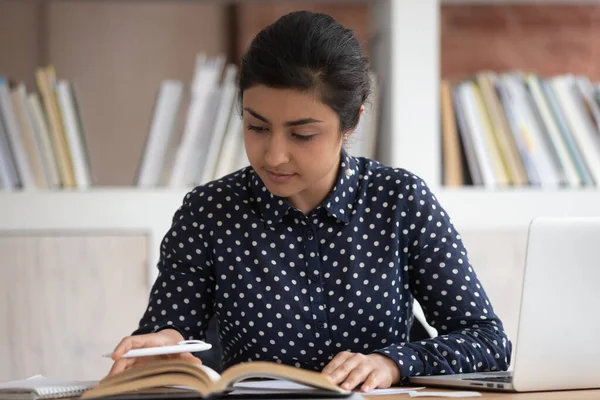 Estudiante indio sentado en el escritorio gire las páginas de información de búsqueda — Foto de Stock