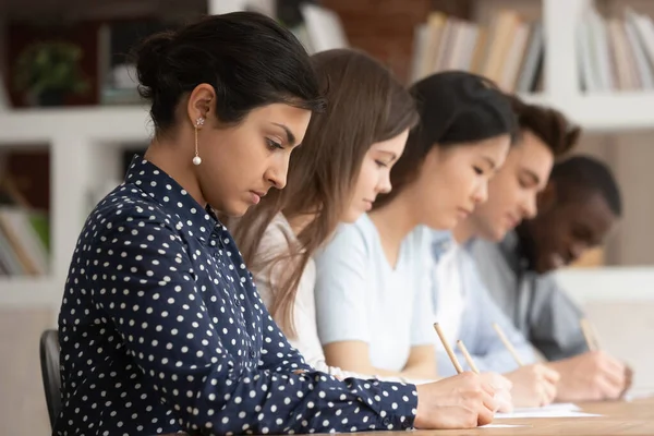 Multiraciala studenter sitter vid skrivbordet skriva på papper gör uppgift — Stockfoto