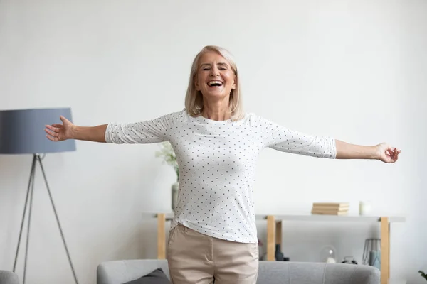 Mujer madura feliz de pie en la sala de estar con los brazos extendidos — Foto de Stock