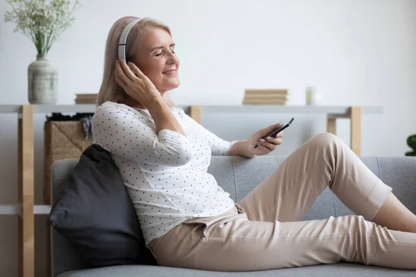 Wanita tua yang tenang memakai headphone mendengarkan musik mobile di rumah — Stok Foto