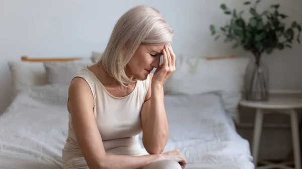 Older woman sit on bed coping with morning headache concept — Stock Photo, Image